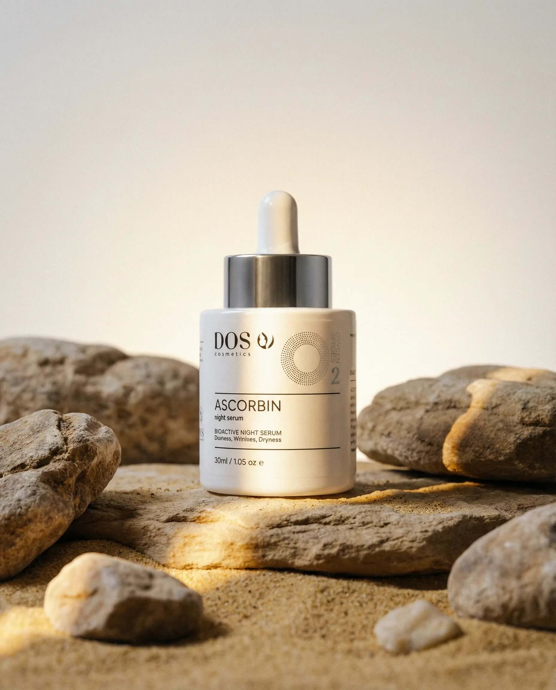 Vitamin C serum Ascorbin in a dropper bottle on sand among rocks for radiant skin renewal and protection. DOS Cosmetics