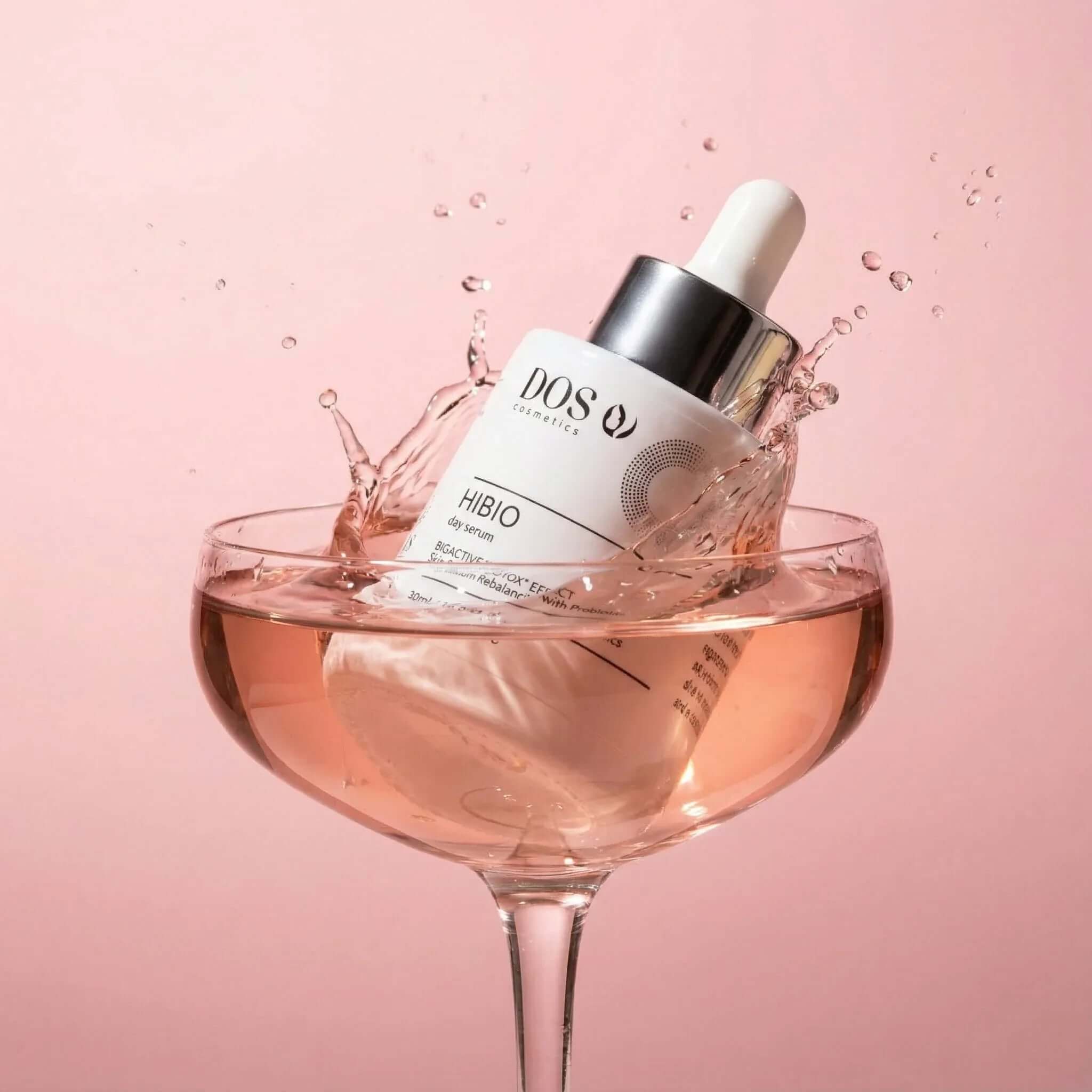 Hyaluronic day serum splashing in a glass with pink background for radiant and hydrated skin. DOS COSMETICS