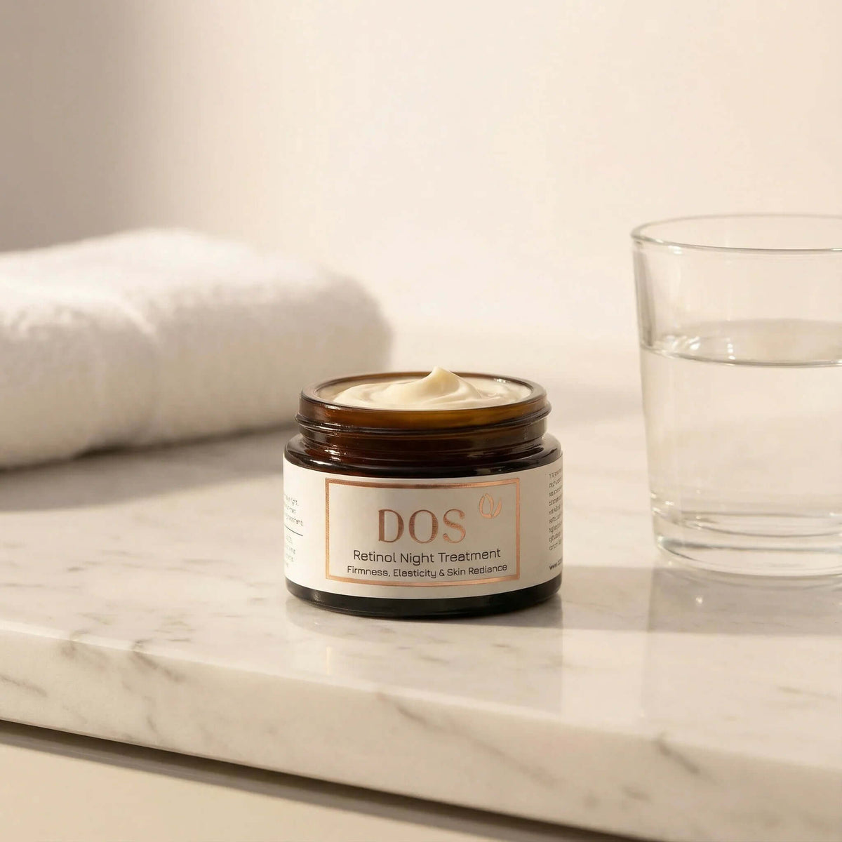 Retinol night cream in a jar on a marble countertop with a glass of water. DOS Cosmetics