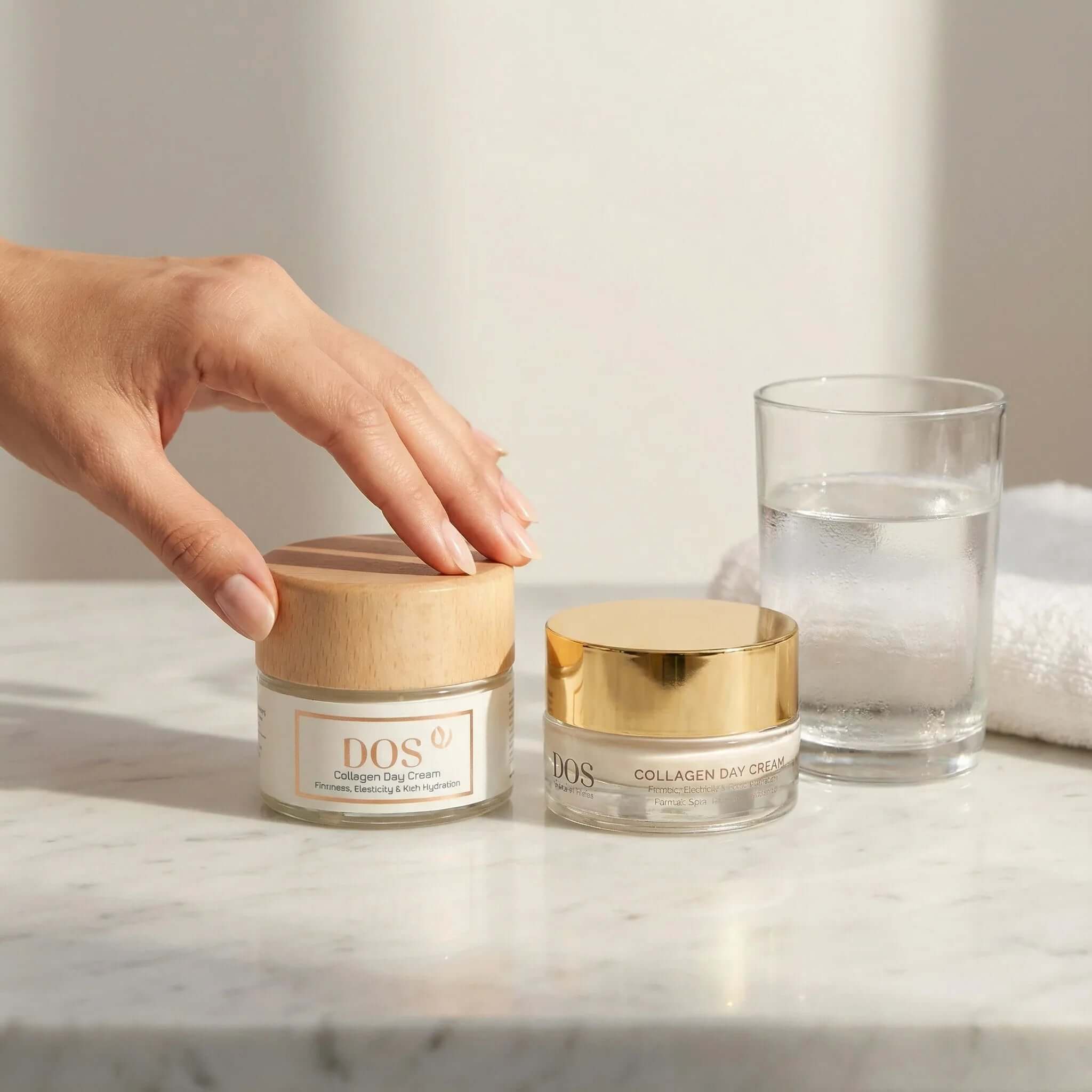 Collagen day cream jars on a marble countertop with a glass of water and a towel. DOS cosmetics