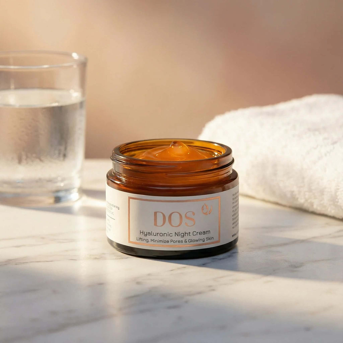 Hyaluronic night cream jar on a marble surface with a glass of water and a towel.  DOS Cosmetics