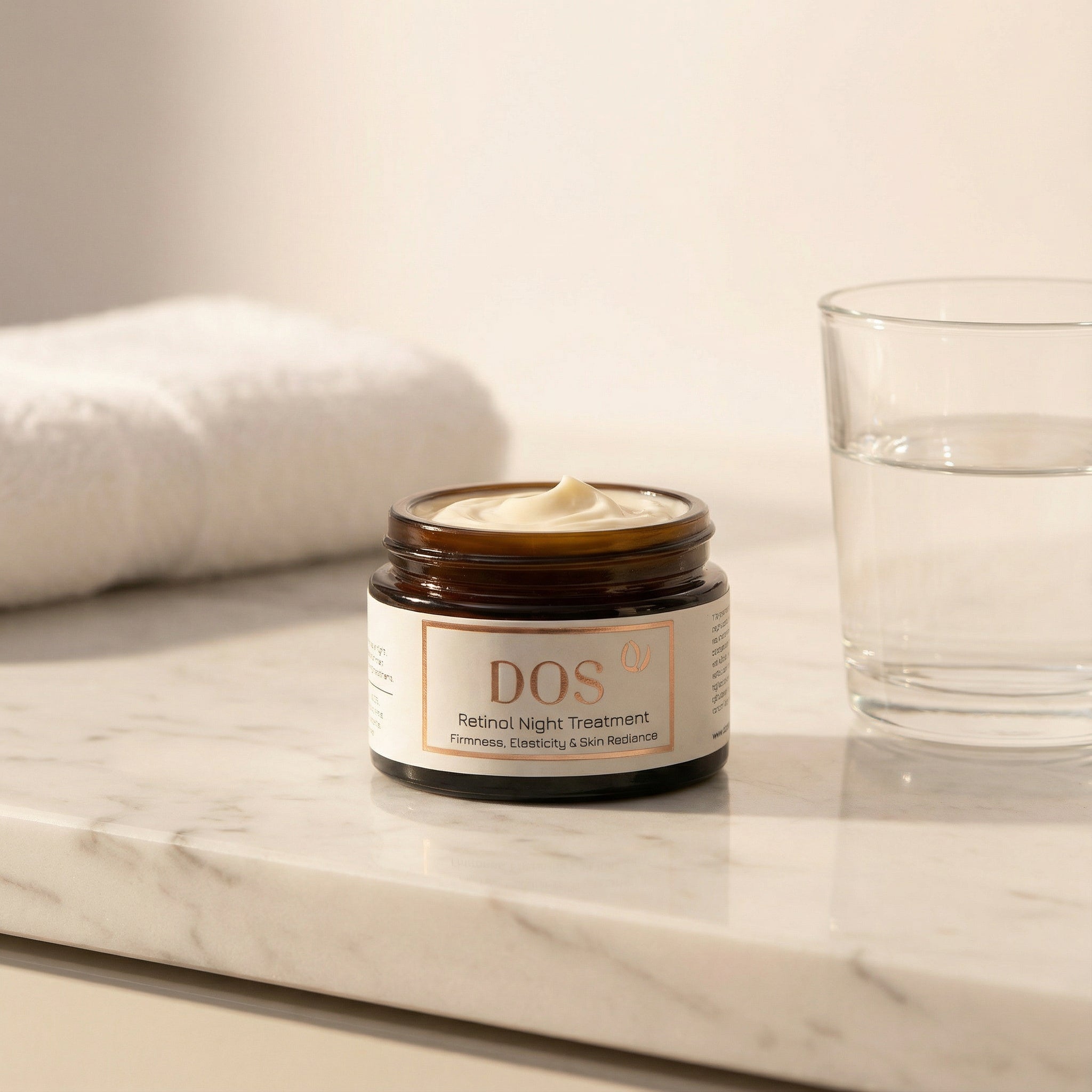 DOS Retinol night cream on a marble surface with a glass and towel in the background showing texture